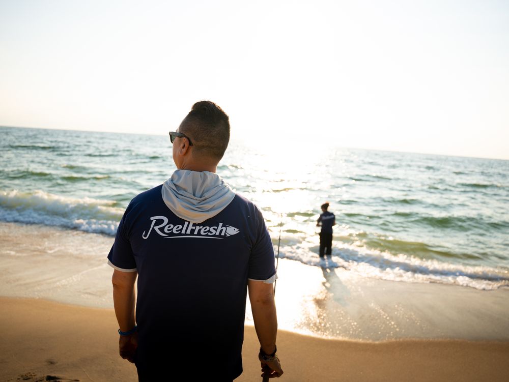 A fisherman on the sand watching a friend wade out into the surf
