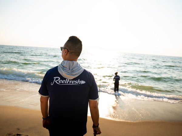 A fisherman on the sand watching a friend wade out into the surf with a rod