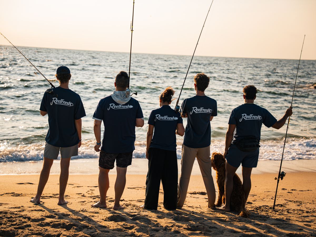 Five members of the tribe, men and women, standing shoulder to shoulder at the water's edge with their rods, a dog beside them